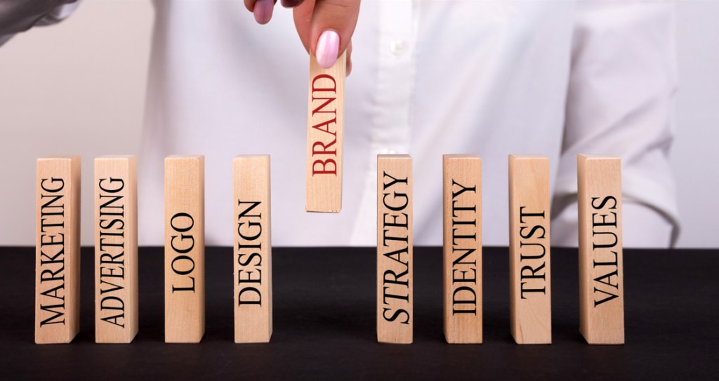 Mão de uma mulher de negócios organizando blocos de madeira, representando a construção consistente de uma marca alinhada a valores, comunicação e experiência do cliente.